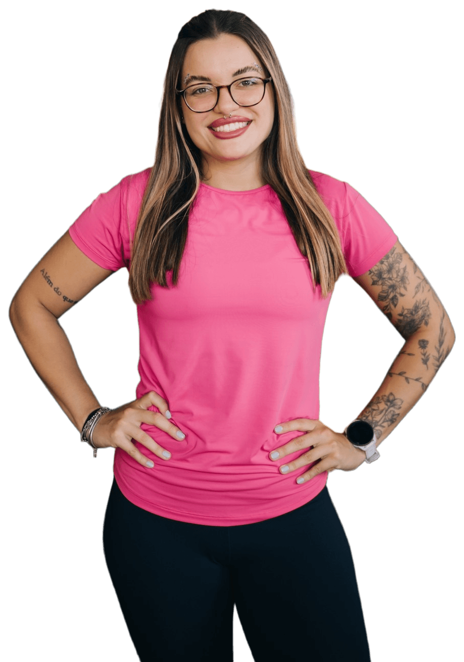 Prof. Maria, de camiseta rosa, sorrindo com as mãos na cintura